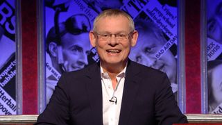 An image of a grinning Martin Clunes hosting HIGNFY.