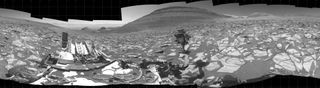 a black panorama of a dry, rocky surface. in view is a rover, which facilitated the photo