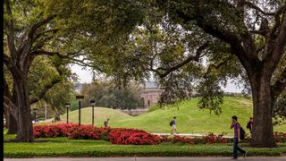 Students pictured walking past two large grassy mounds on the LSU campus