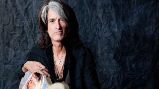 Joe Perry sitting on a stool with a guitar