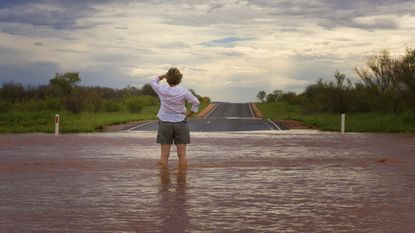 A woman stands in floodwaters looking toward an unflooded road ahead.