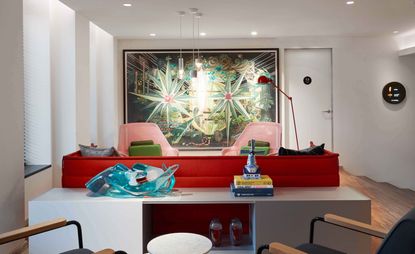 Lounge area featuring a red sofa, pink chairs and a large piece of geometric artwork