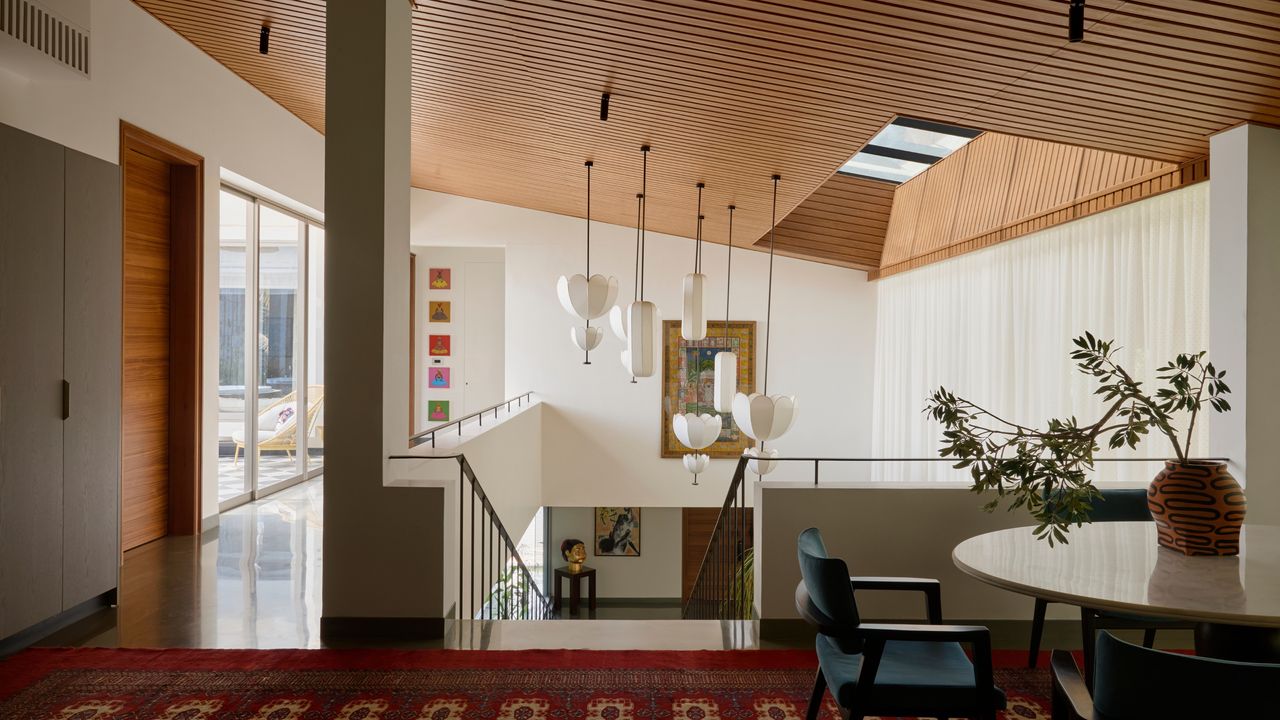 An upstairs area with an open concept staircase and skylight. The ceiling is wooden with a cluster of lantern pendant lights hanging by the staircase. There is art hung on the walls on both the upper and lower levels.