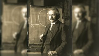 Albert Einstein stands next to a blackboard