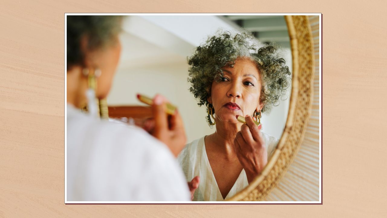 Image of woman applying lipstick in the mirror in a frame against a beige watercolour-style background 