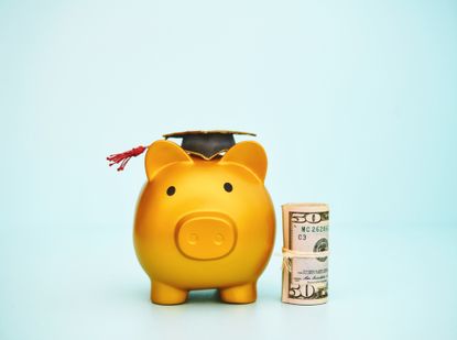 Gold piggy bank wearing a graduation cap and standing next to a roll of dollars.