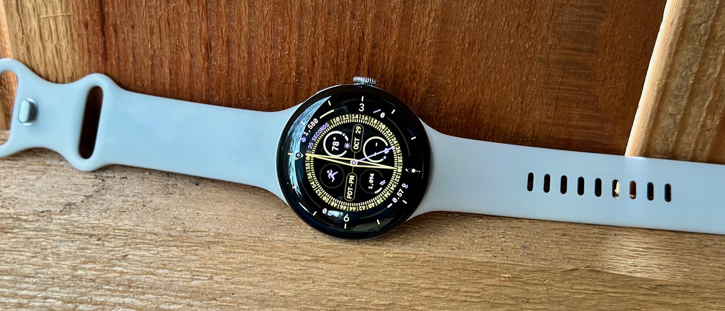 A photo of the Google Pixel Watch 4 sitting on a brown fence board, showing the Expedition watch face.