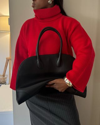 Woman wears red jumper, pinstripe skirt, carries black bag