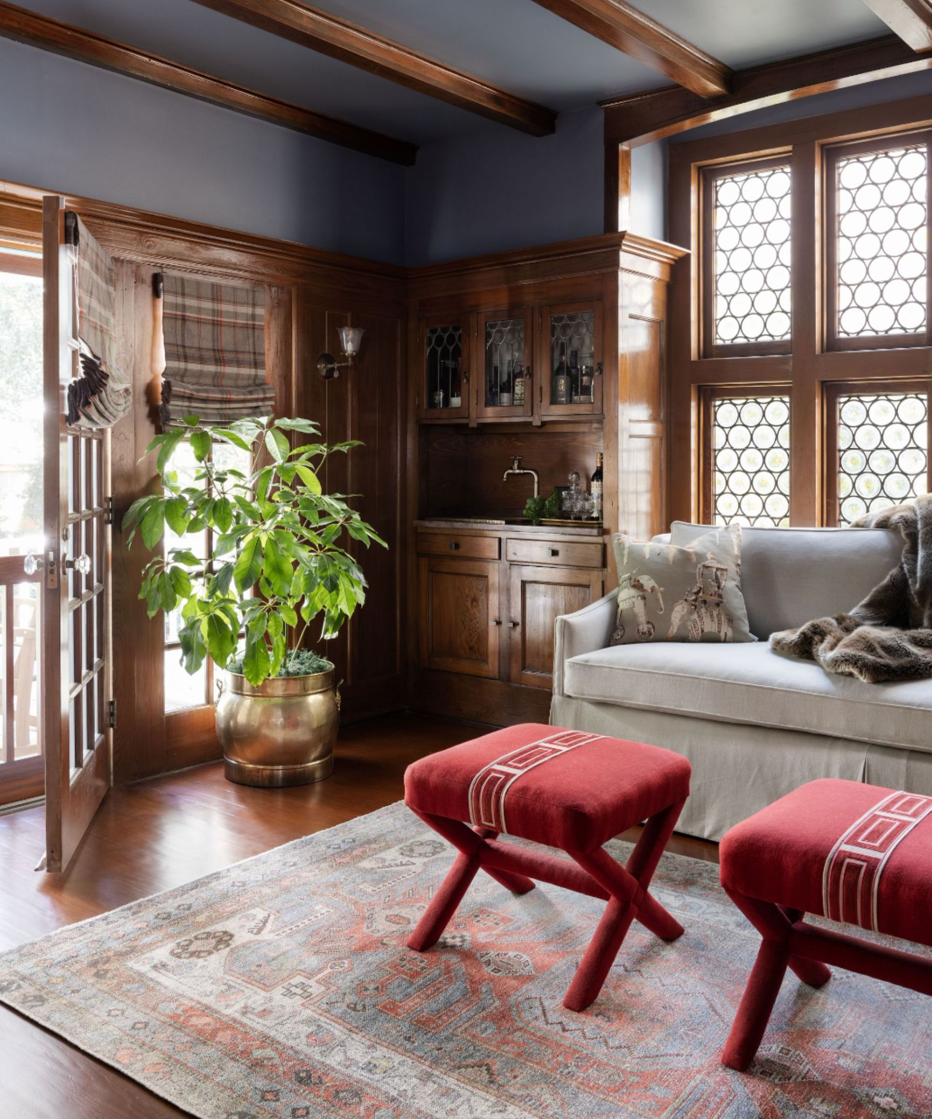 A keep room with dark walls, wood beams, a built in bar cabinet, a gray sofa, and a Persian-style rug