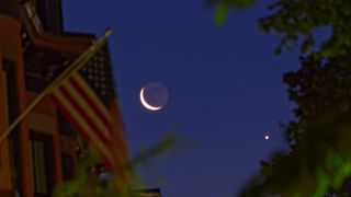 he rising moon in conjunction with Venus is framed on the left by brick townhouses with wooden dormers and an unfurled American flag in Boston's historic South End. Leafy treetops complete the framing on the right. The photo was taken at the start of nautical twilight.