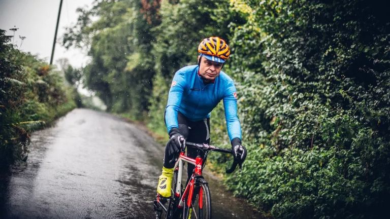 Best waterproof cycling jackets. Image shows a man cycling in the rain on a red and white bike