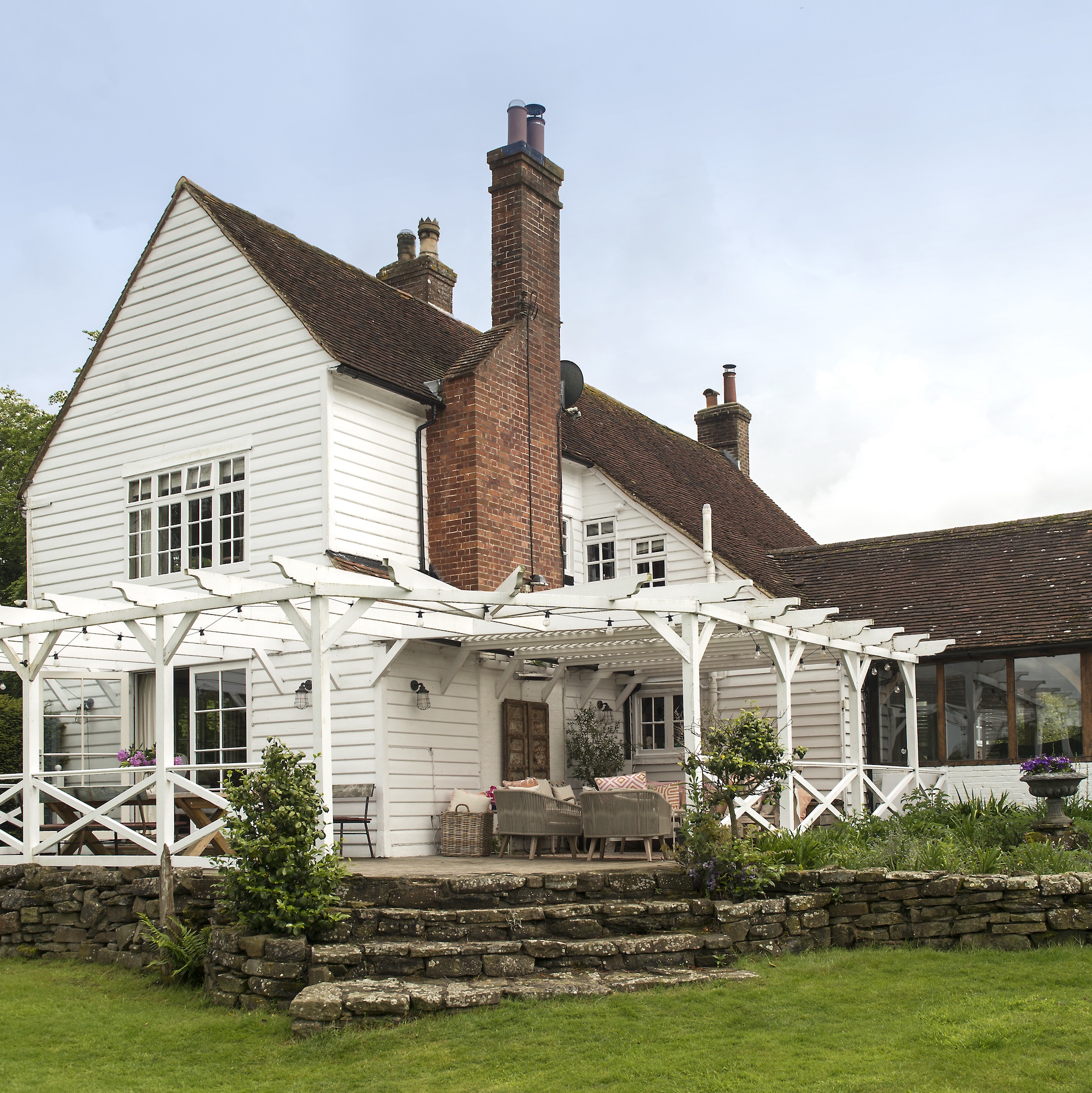 Exterior of white clapboad house with white painted wood pergola and veranda