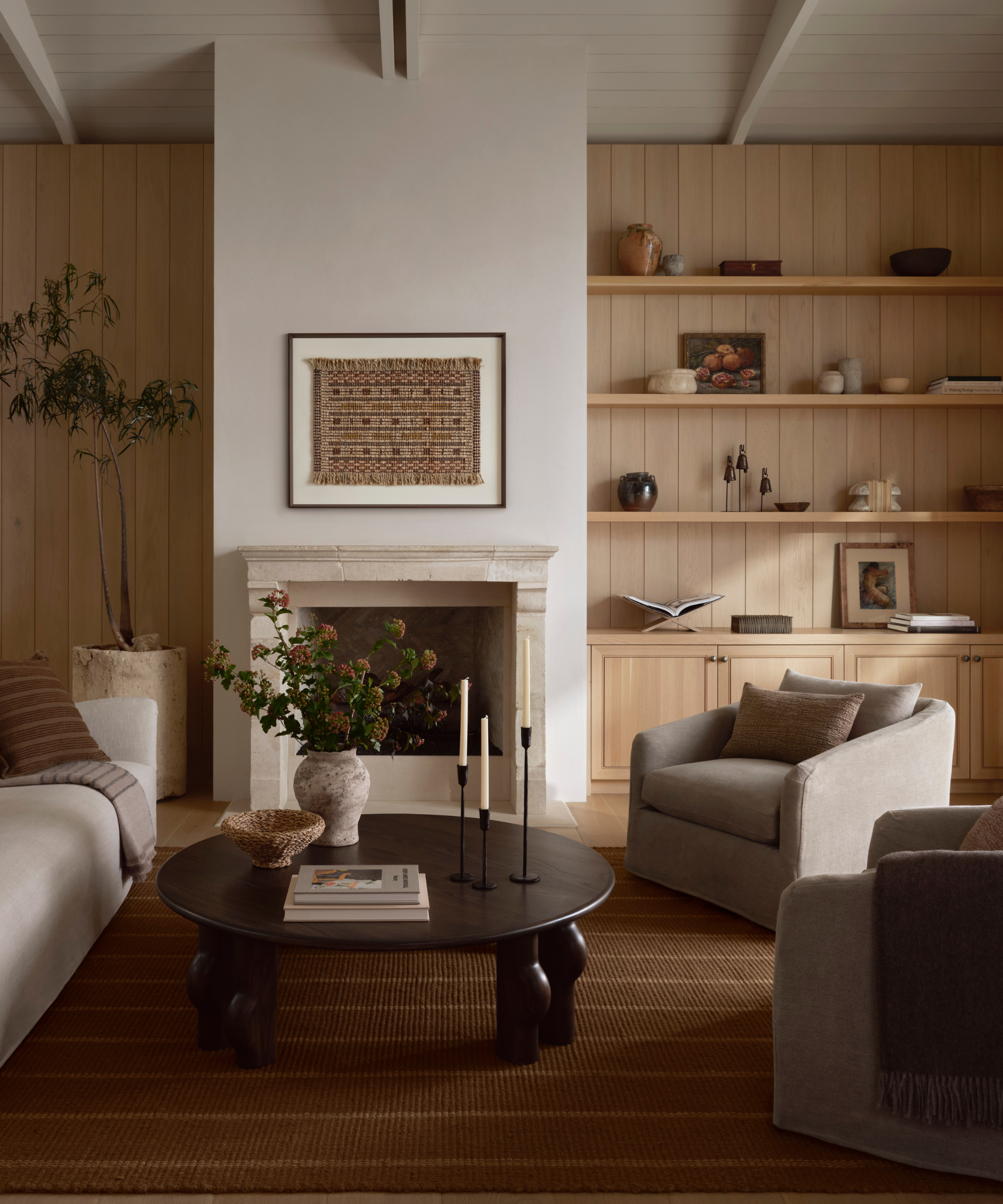 a warm living room with wood paneling on the walls, a round wood coffee table, two accent chairs, a couch, and a striped rug on the ground
