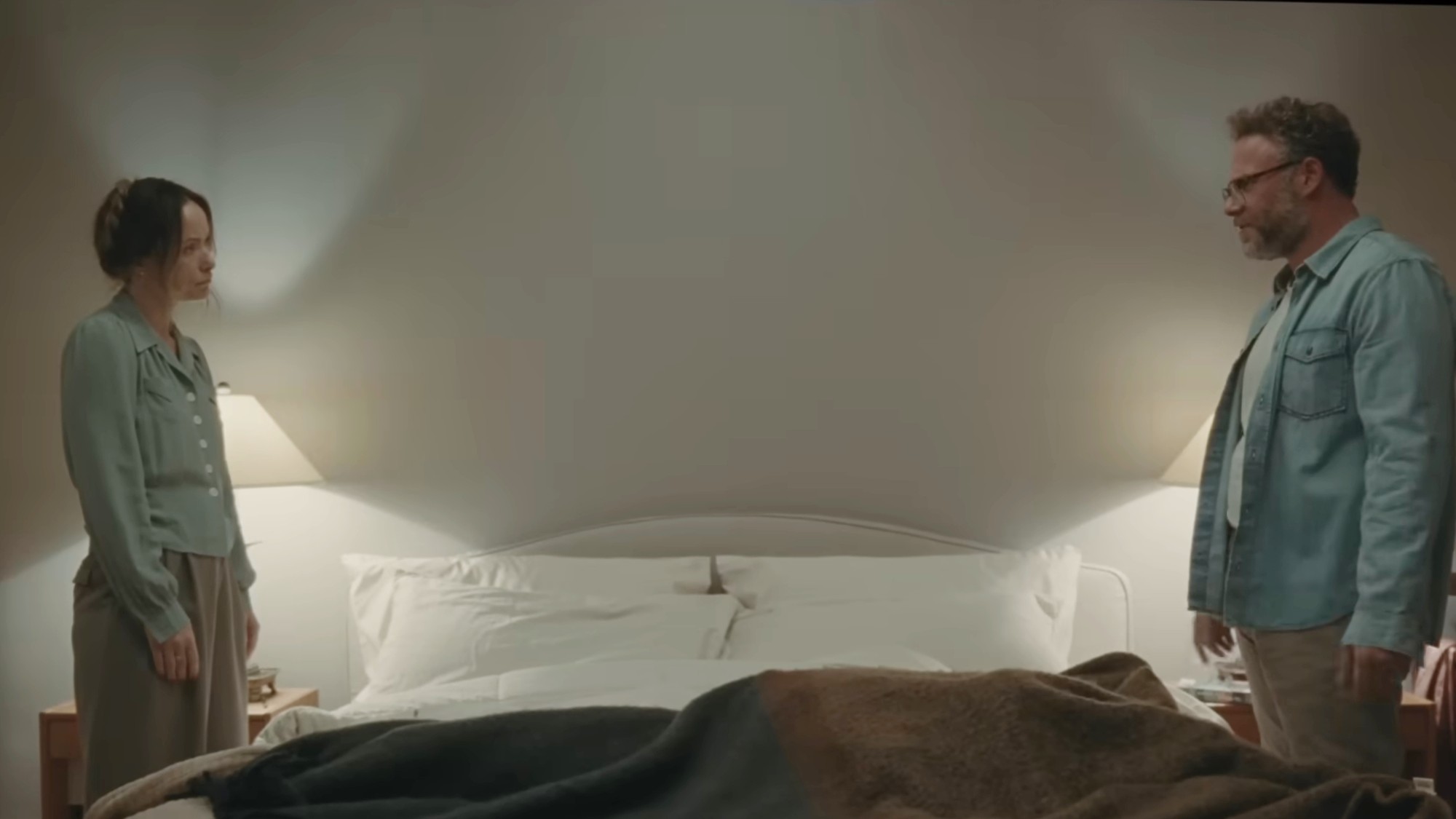 Seth Rogen and Olivia Wilde looking at each other across a bed in The Invite.
