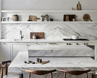 White kitchen with marble backsplash and countertop and multi level island