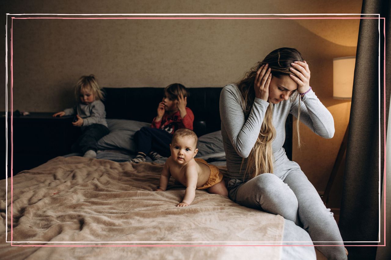 A woman with her head in her hands sat on a bed next to three children