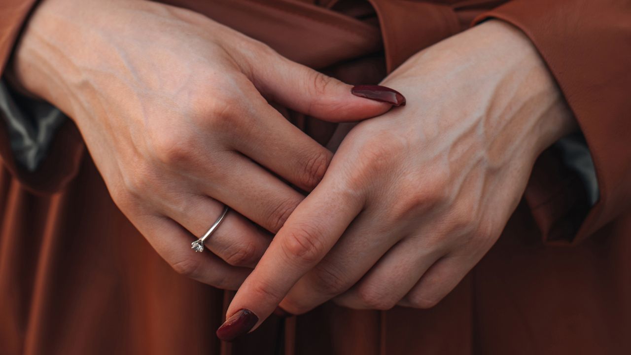 A person wearing a brown coat, with their hands featuring brown nail designs