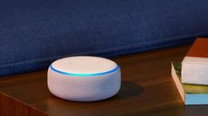 Amazon Echo Dot (3rd Gen) in white on dark wood surface behind blue sofa