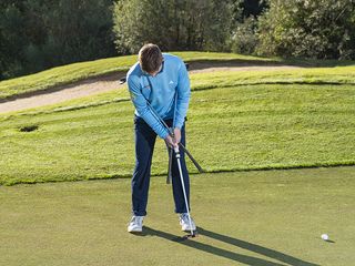 Alex Elliott demonstrating a putting technique drill using two clubs under armpits