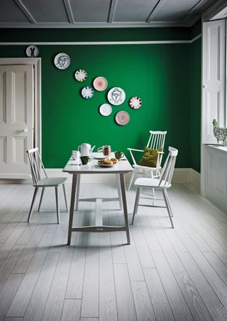 Gallery wall with plates on a green wall with a white long dining table on a painted floor