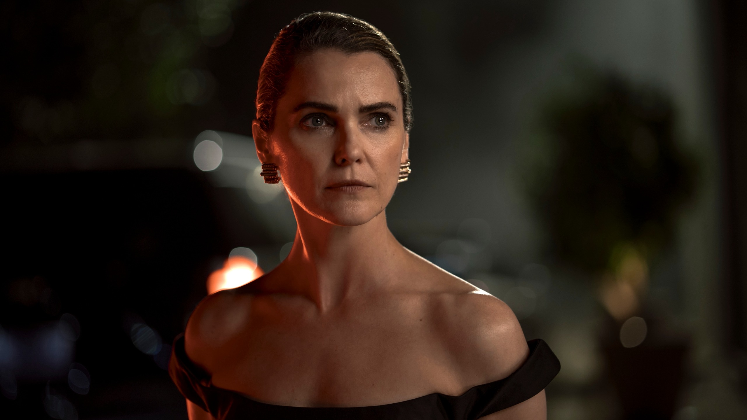 Keri Russell as Kate Wyler wearing a black off the shoulder dress with her hair tied up.