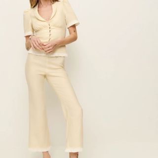 A model wearing a pale yellow two piece trouser suit posed against a light wall