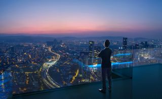 An executive at the top of a building looking out over a city at twilight