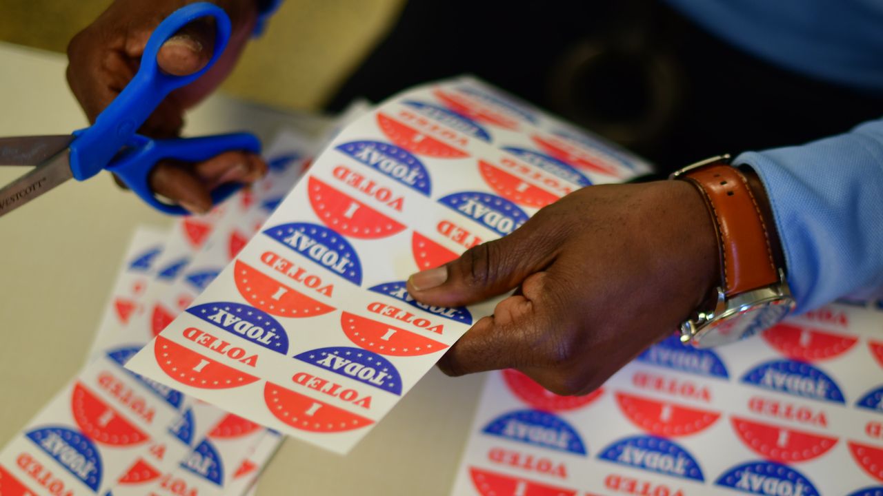 A volunteer cuts out &amp;quot;I VOTED TODAY&amp;quot; stickers for voters queueing outside a polling station