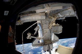 Discovery STS-133 astronaut Steve Bowen stands at the tip of the International Space Station's Canadian robotic arm, with the Earth and space shuttle in the background, during the second spacewalk of his mission on March 2, 2011.