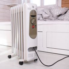oil-filled radiator in a wood clad room, in front of a day bed with a blanket
