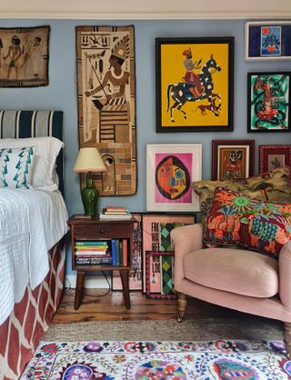 bedroom with blue walls pink chair and colorful embroidered artwork