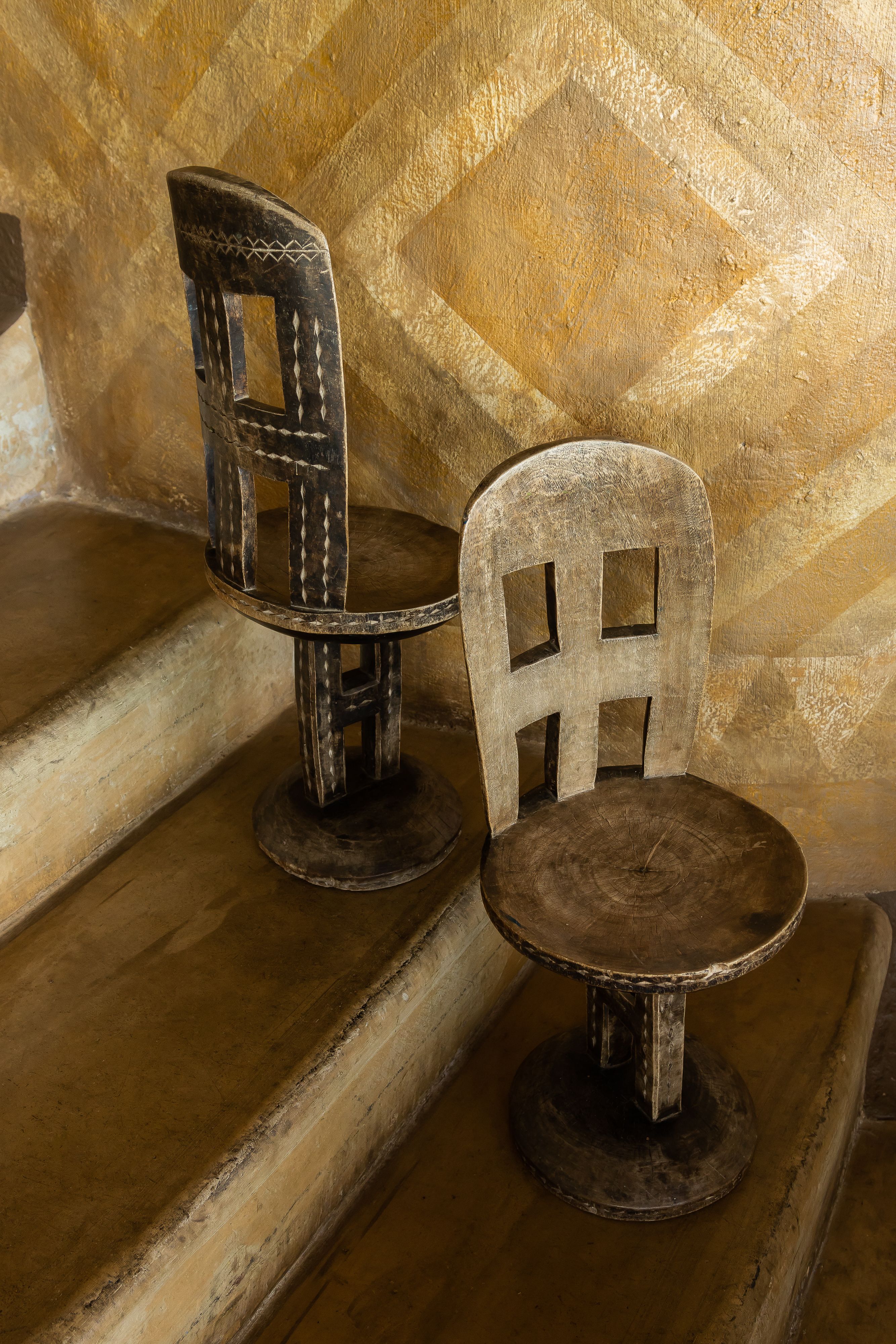 Some artisanal furniture, including wooden chairs with a highly textural, sculptural feel, and a lacquered black table with wood and rattan seats, are portrayed inside a naturally lit hotel room.