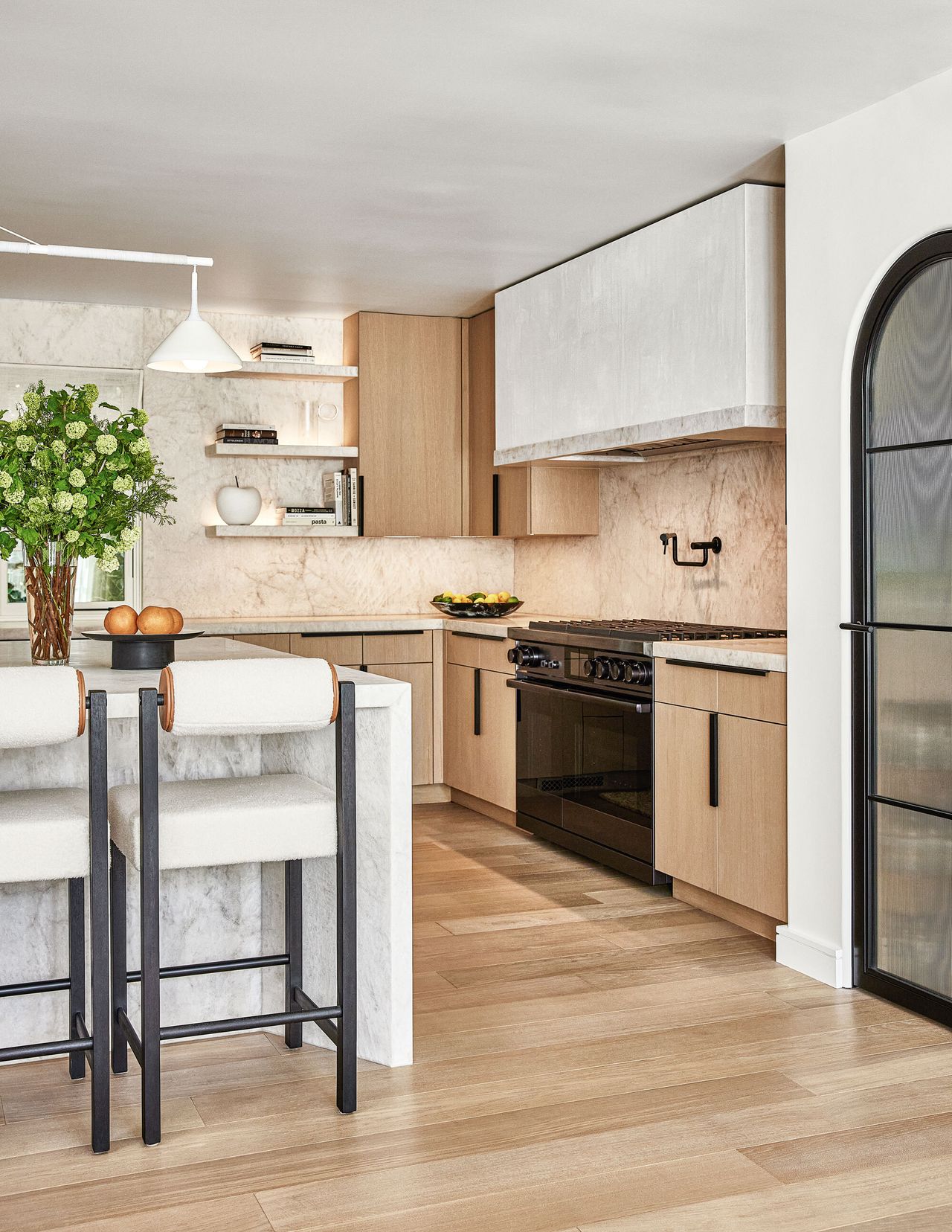 A black range stove and stone detailing and waterfall island in a neutral kitchen renovation