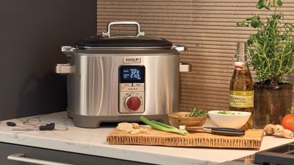 A Wolf Gourmet Multi-Function Cooker on a kitchen countertop with a chopping board and ingredients 