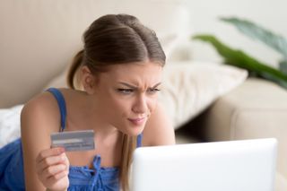 Young woman holding credit card and looking at laptop screen with skeptical expression.