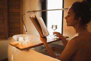A woman reading in the bath with a glass of wine