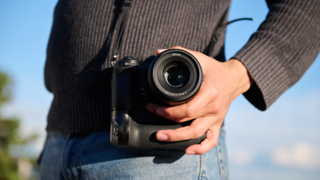 A person holds a DSLR on a strap over their shoulder