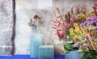 Flower displays and glass-brick podiums against a bare concrete wall and blue floor