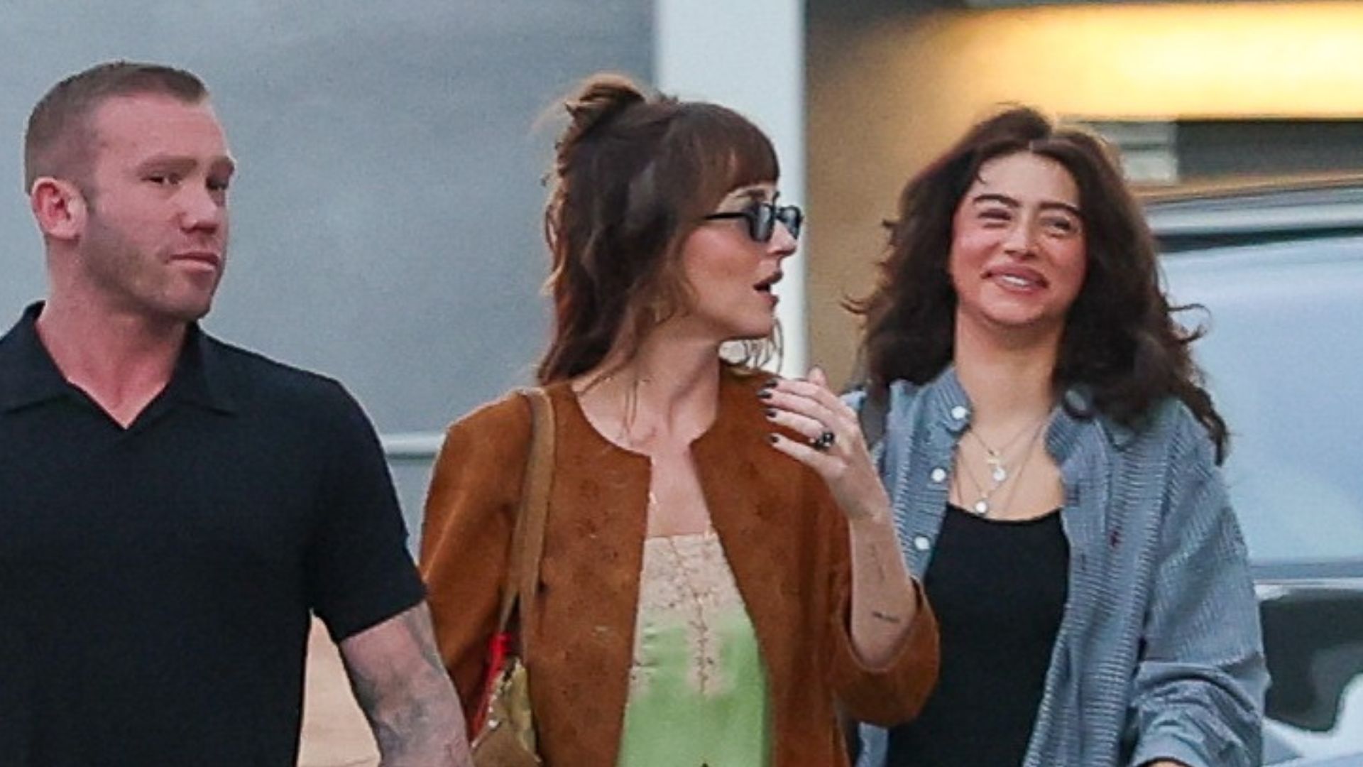 An image of Dakota Johnson wearing a green slip dress, suede jacket and black ballet flats. 