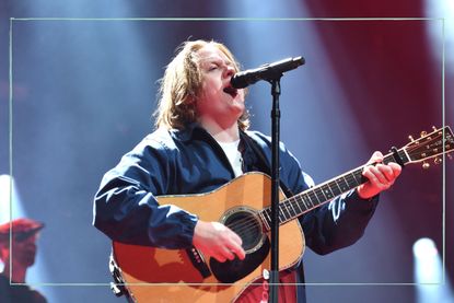 Lewis Capaldi singing into a microphone and playing a guitar