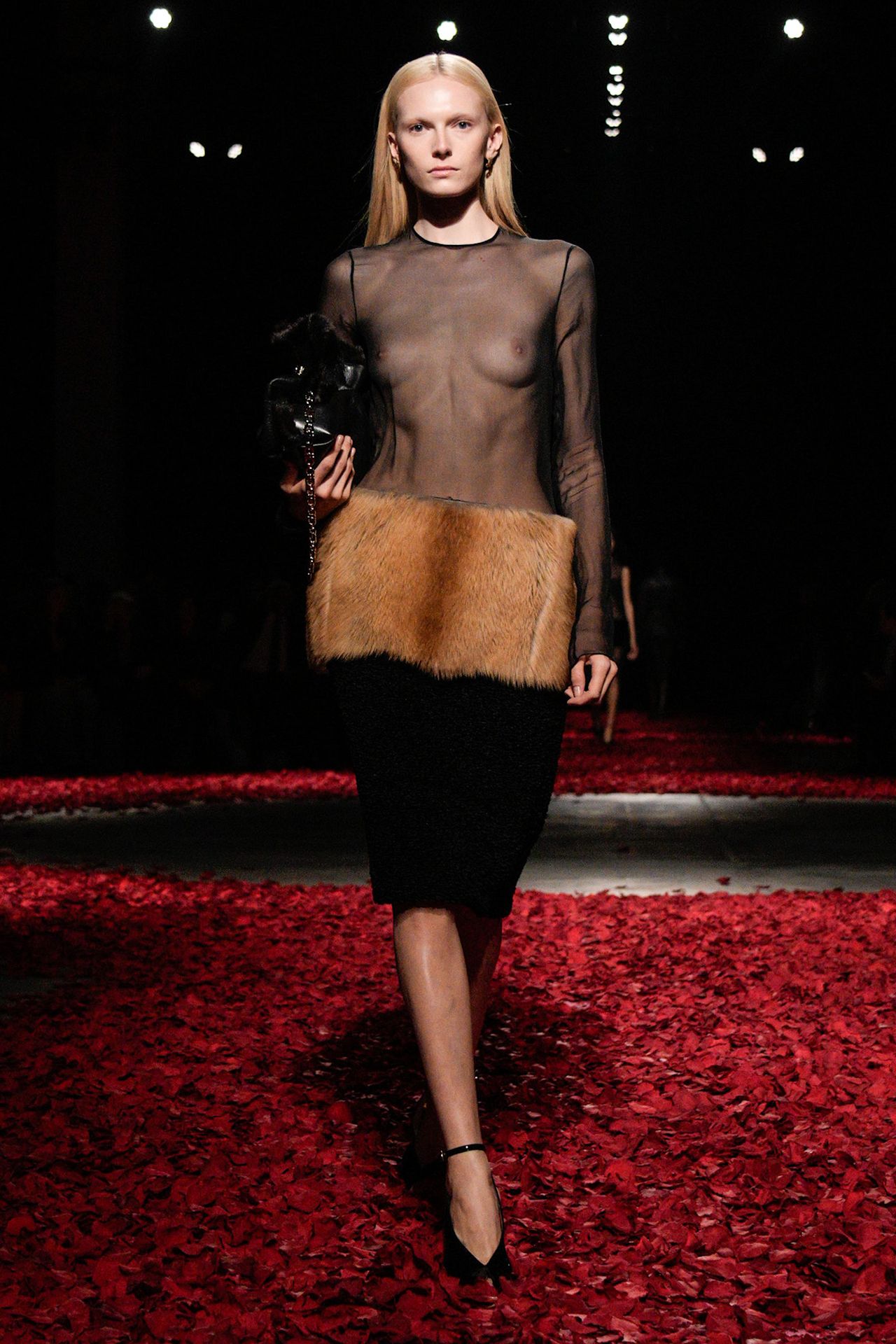 A model walking in the Ferragamo F/W 25 runway show wearing a sheer black top with a black fur skirt.