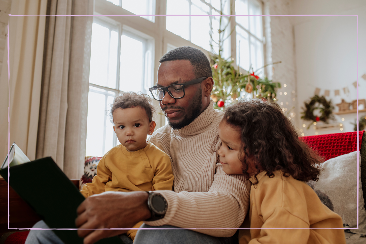 Dad with daughters reading book on sofa at Christmas