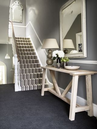 Hallway with console table and mirror and black carpet plus staircase with striped carpet
