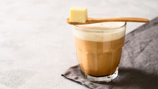 A cup of bulletproof coffee with a spoon of butter over the top on a simple, monochrome background