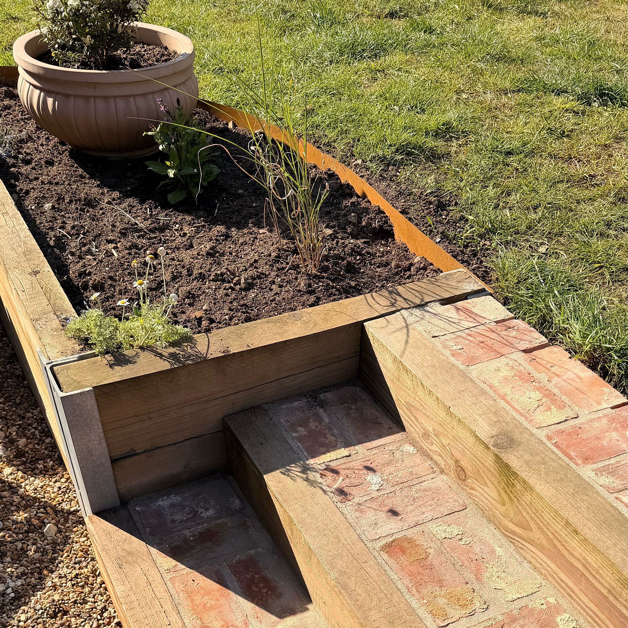 Red brick and wooden steps in garden attached to raised bed