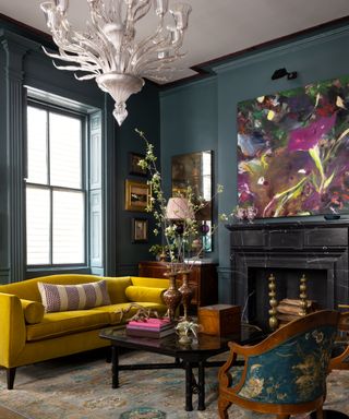 dark blue living room with bright yellow couch, vintage rug, artwork, antique chair, vintage chandelier, modern painting on wall, eclectic furniture,