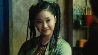 Lana Condor smiles sharply while she sits at a table in Alita: Battle Angel.