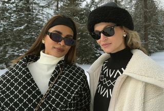 Two women dressed in black and white winter accessories.