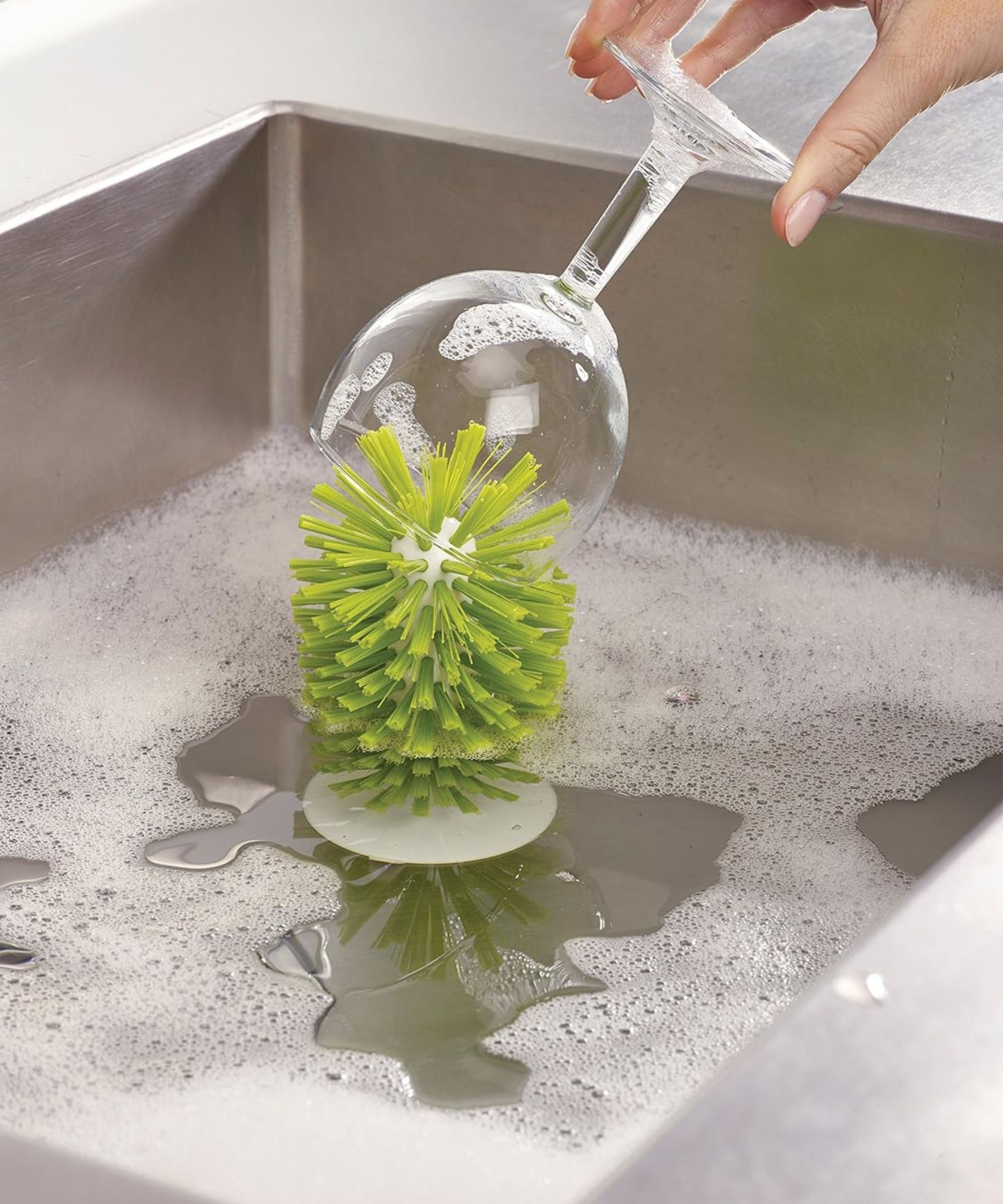 Joseph joseph sink-up brush in a silver sink with a hand washing a wine glass