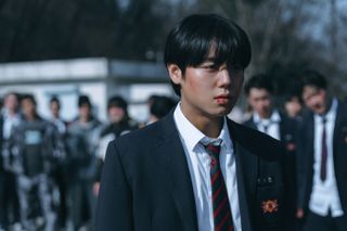 A high school boy with a bruised face stands in front of a crowd of students, in 'Weak Hero Class 2.'